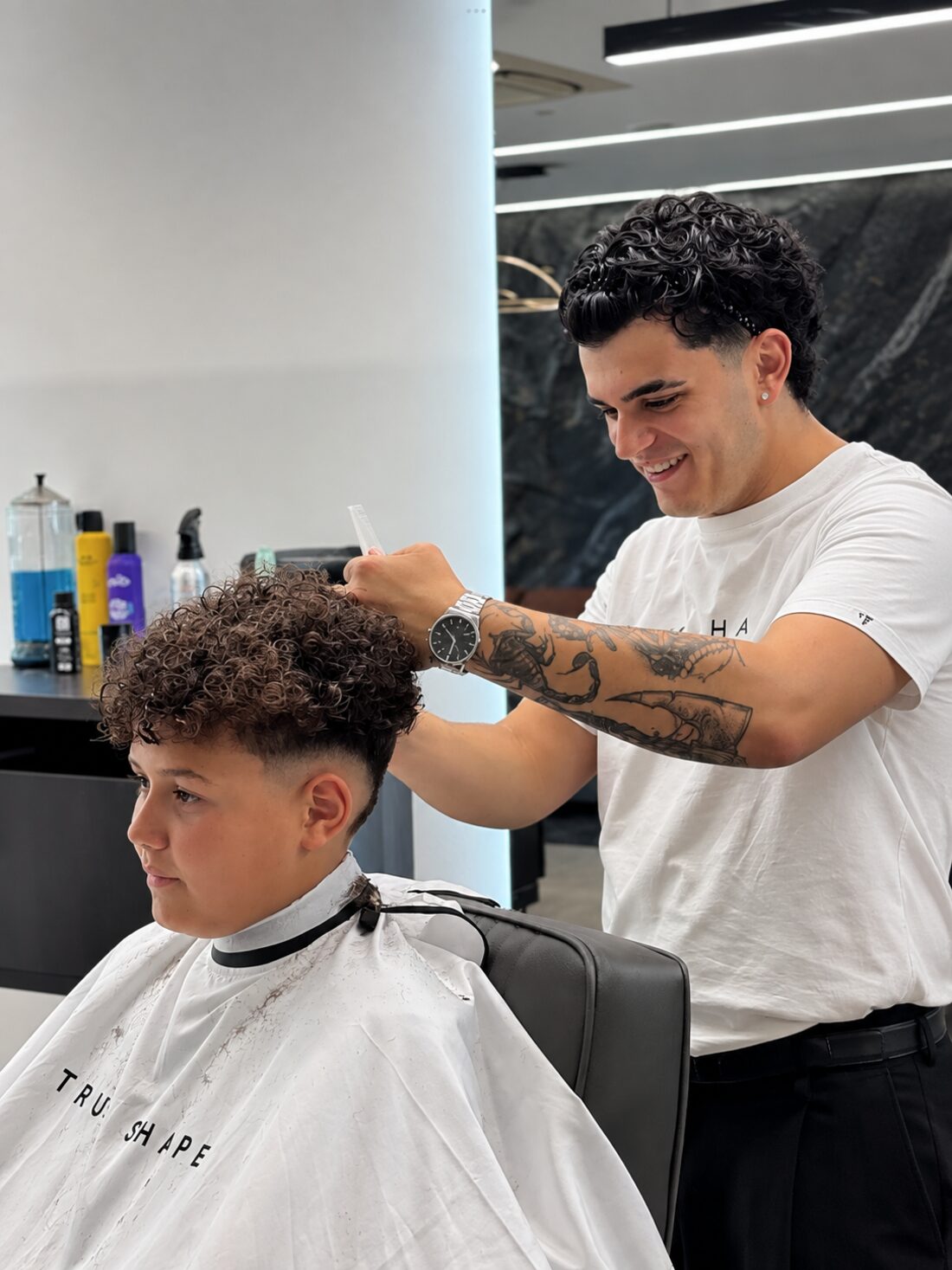 Barbeiro a conversar e a sorrir enquanto corta o cabelo a um cliente jovem